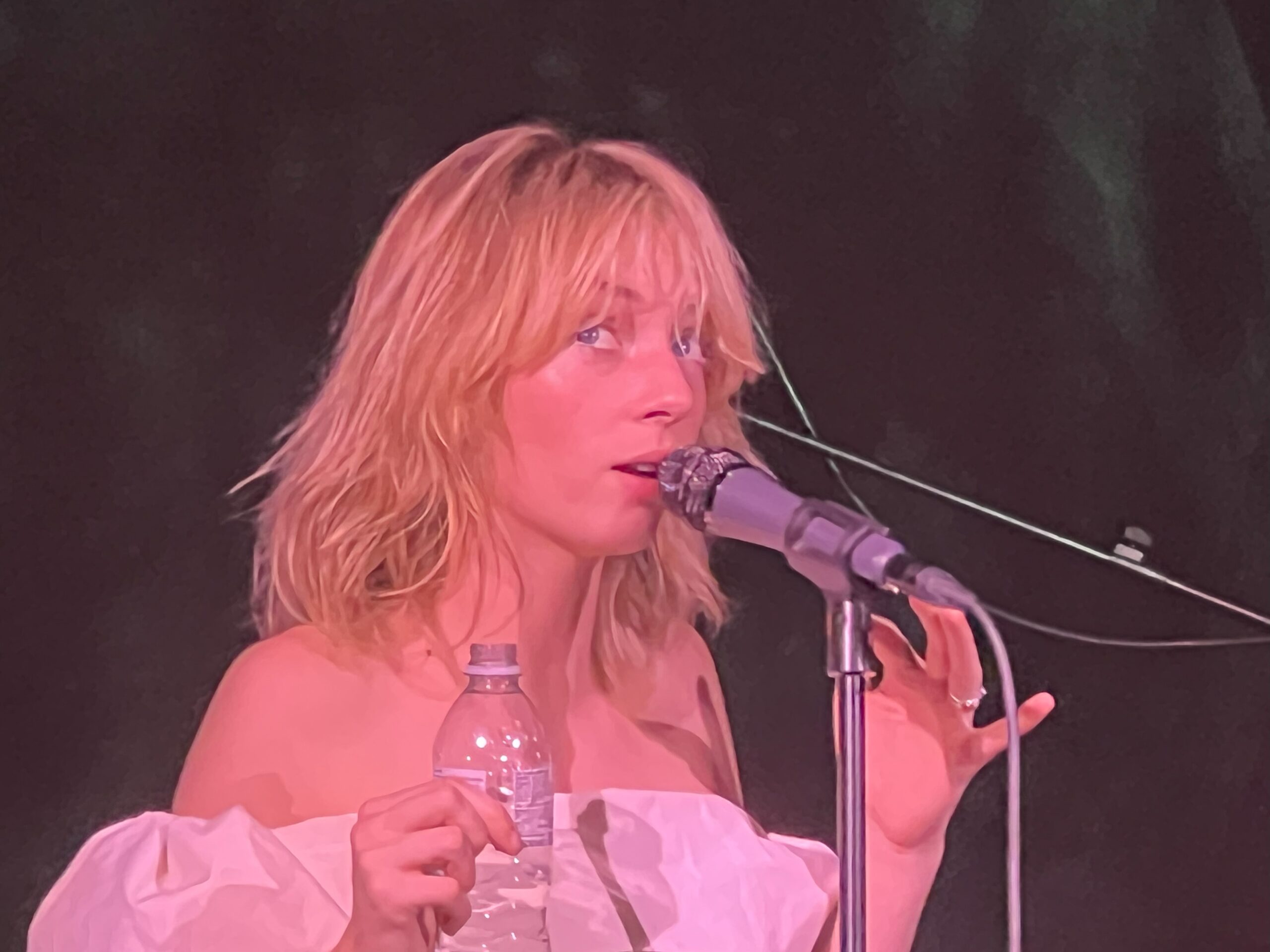 Photo of Maya Hawke with a microphone performing a live gig.